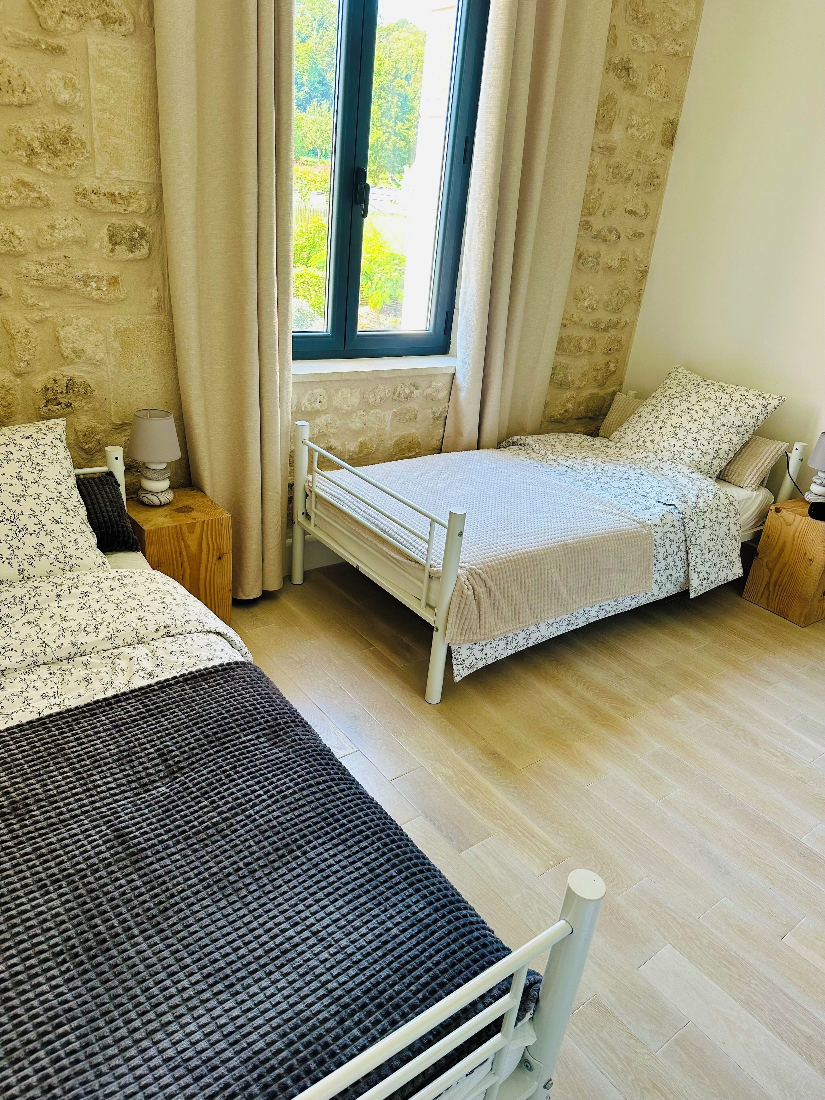 Een slaapkamer met twee bedden, een raam met gordijnen, een lamp en een stenen muur.