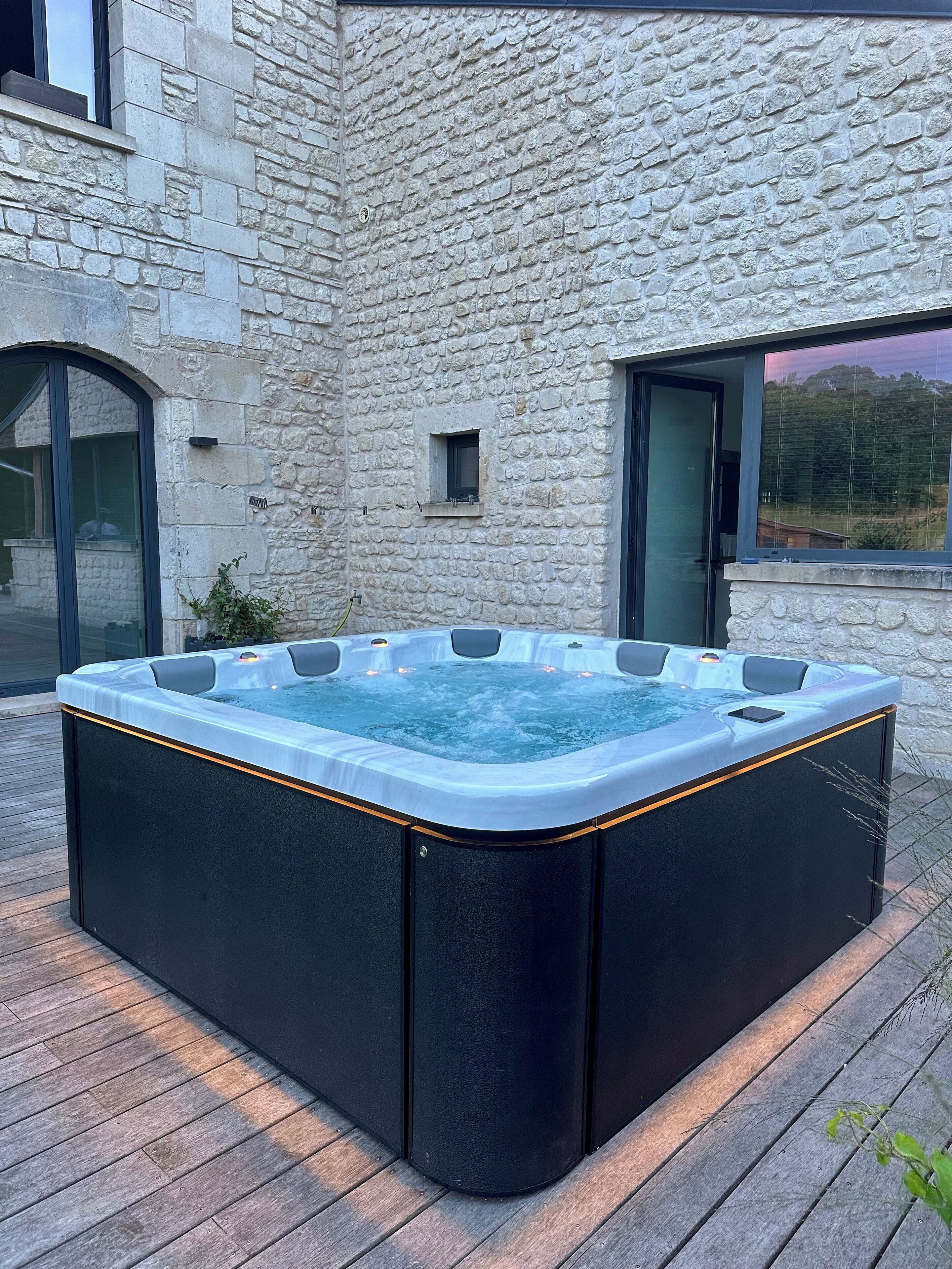 Un jacuzzi en un entorno al aire libre con una pared de piedra y una terraza de madera.