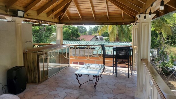 A covered outdoor area with a table and chairs, a sink, and a view of a green-roofed building in the background.