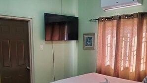 A bedroom with a bed, a television mounted on the wall, a door, and a window with curtains.
