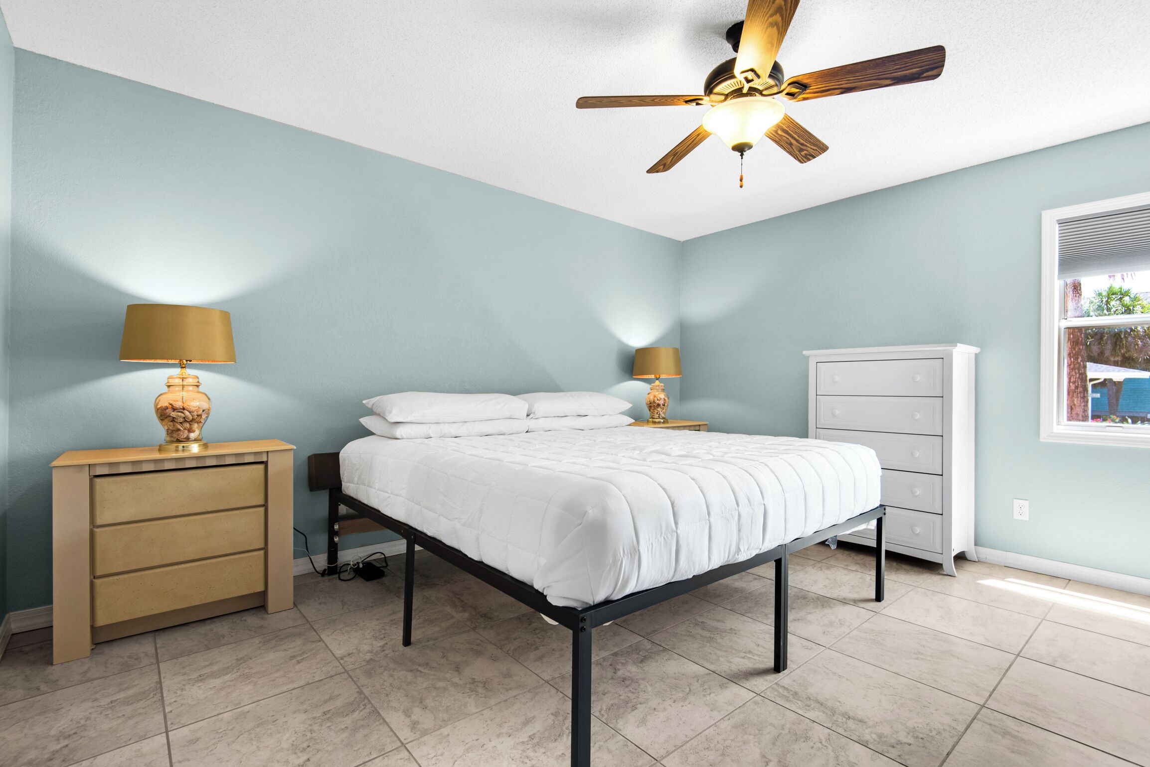 A bedroom with a bed, nightstands, a dresser, a ceiling fan, and a window with blinds.