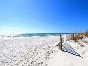 Een zandstrand met een houten omheining en schaarse begroeiing.