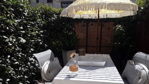 An outdoor patio with a table set for two, striped cushions, and a decorative umbrella. - Studio Accès Direct Plage (Arcachon)