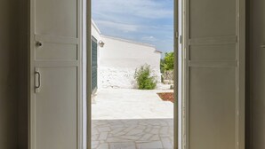 Une porte ouverte donnant sur une cour intérieure avec un bâtiment blanc, un chemin de pierre et un ciel dégagé.