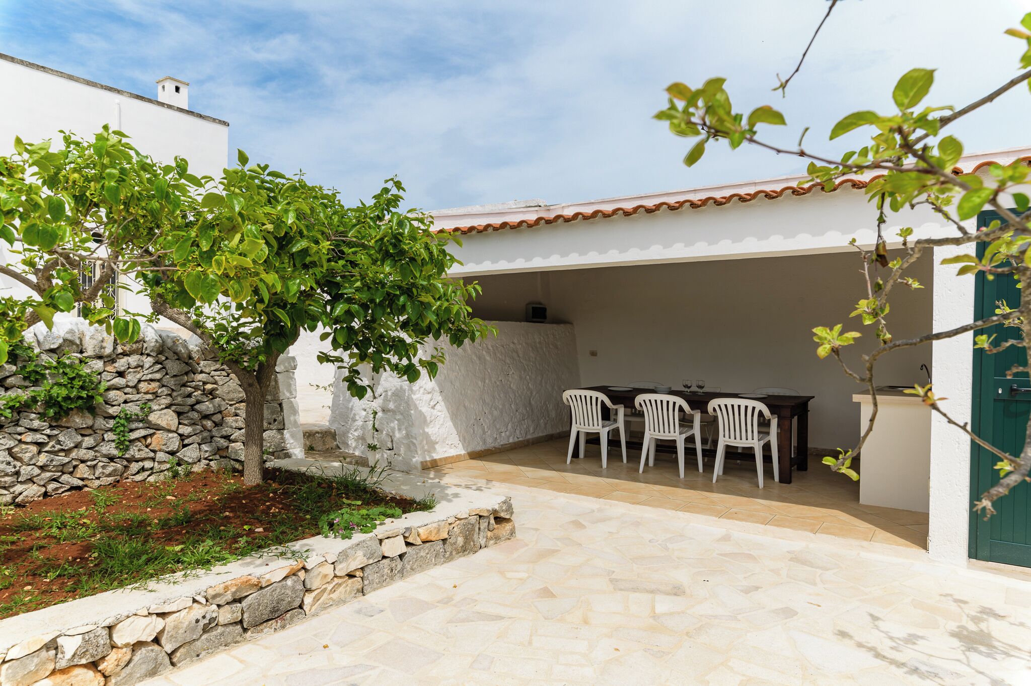 A patio area with a stone wall, a tree, and a table with chairs.