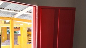 Una habitación con cama, ventana y puerta roja.