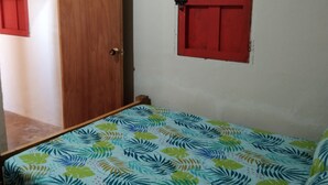 Una habitación con una cama, una puerta de madera y un persiano rojo.