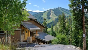 A lodge with a stone facade, a wooden front door, and a stone porch. It is surrounded by trees and has a view of a mountain range.