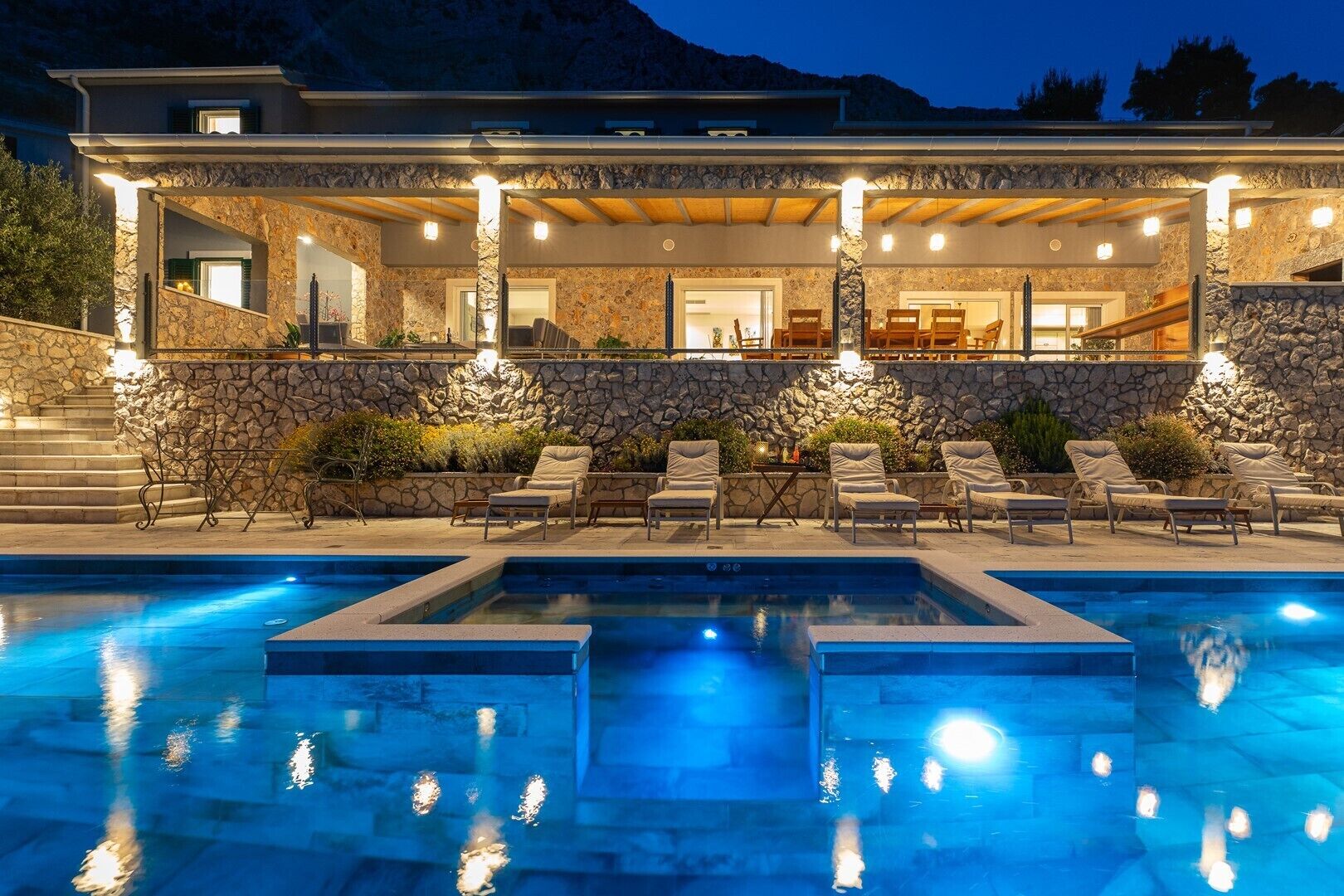 Una casa moderna con fachada de piedra, piscina y mobiliario de exterior.