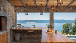 A rustic kitchen with a stone wall, wooden counter, and a view of the sea. - Seaview Villa Granda Lokva (Lokva Rogoznica)