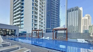 Una piscina en la azotea con sillones de descanso y una terraza de madera, rodeada de edificios altos.