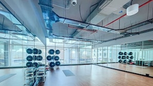 Un gimnasio espacioso con suelos de madera, equipamiento de ejercicio y amplias ventanas con vistas a la ciudad.