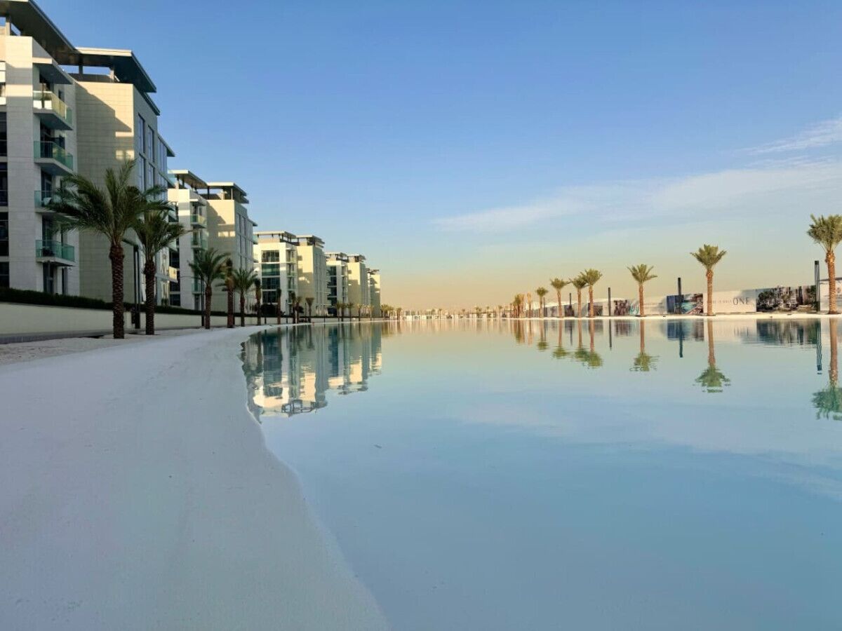 A beachfront hotel with a pool reflecting the buildings and palm trees.