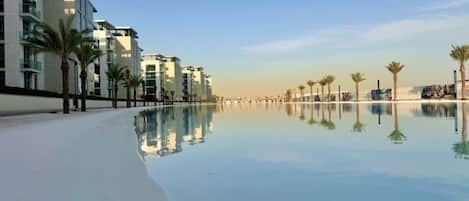 A beachfront hotel with a pool reflecting the buildings and palm trees.