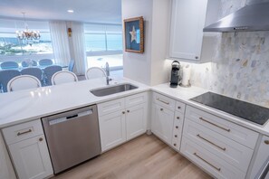 A modern kitchen with a dishwasher, a coffee maker, and a view of the beach.