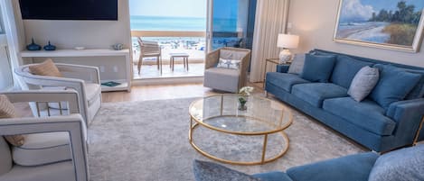 A modern living room with a view of the beach, a flat-screen TV, and a comfortable seating area.
