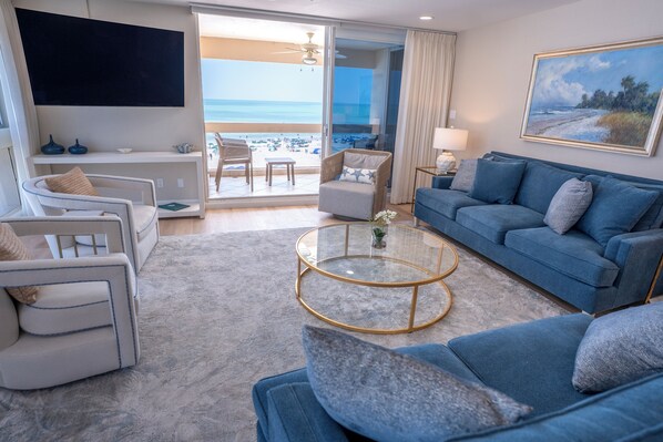 A modern living room with a view of the beach, a flat-screen TV, and a comfortable seating area.