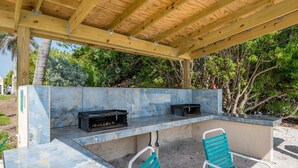 Eine Terrasse im Freien mit einer Holzw pergola, einer Marmorarbeitsplatte, zwei schwarzen Grillen und zwei türkisfarbenen Stühlen.
