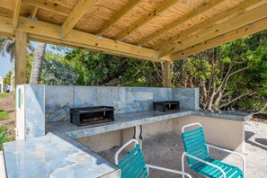 An outdoor patio with a wooden pergola, a marble countertop, two black grills, and two turquoise chairs.