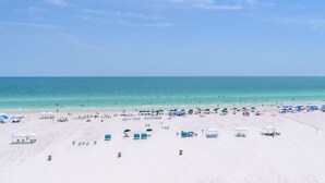 A beach with white sand, clear blue water, and umbrellas.