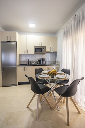 A modern kitchen with a dining area, featuring a refrigerator, microwave, and a table set for four.