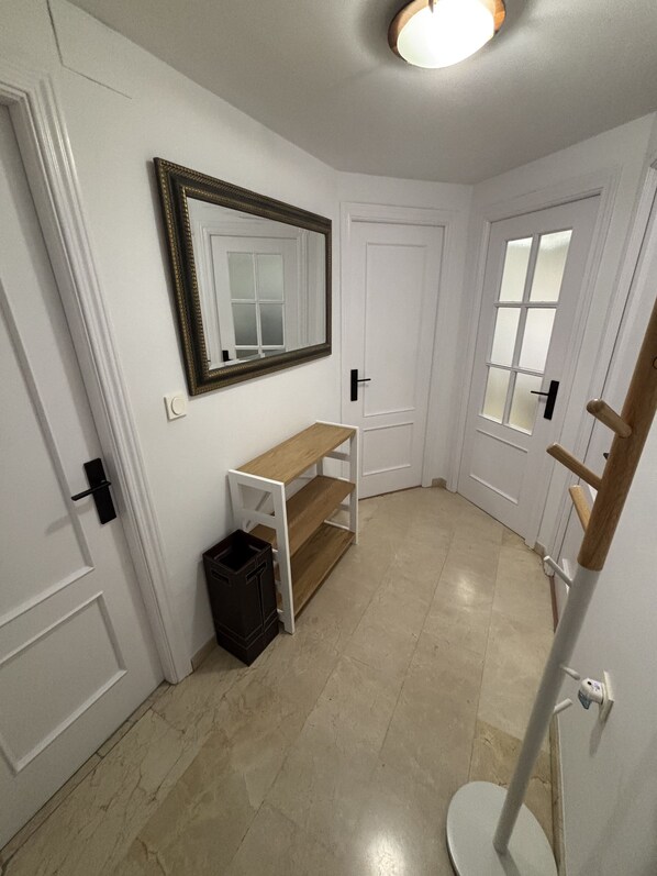 A hallway with white walls, a wooden bench, a black trash bin, and a white door with a frosted glass window. - San Jerónimo 18 Apartment (Granada)