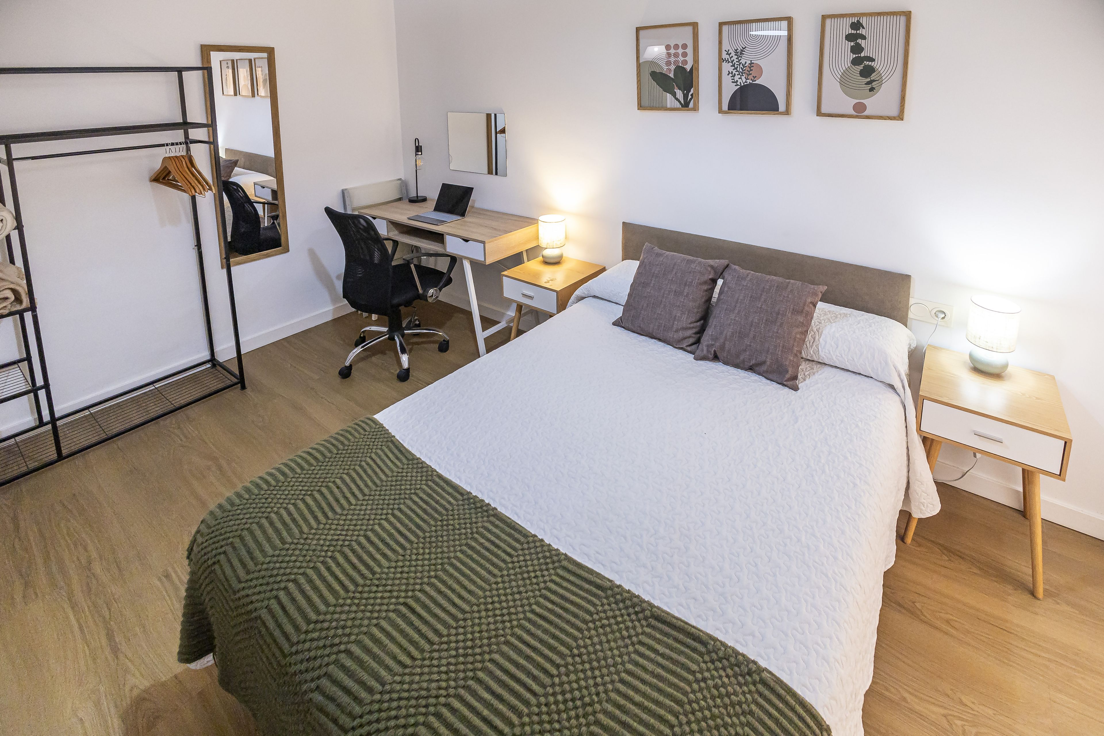 A hotel room with a bed, a desk, a chair, a wardrobe, and artwork on the wall.