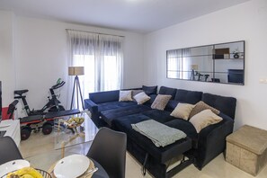 A living room with a dark blue sofa, a dining table with plates and utensils, a bicycle, and a large mirror on the wall.