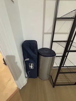 A corner of a room with a white wall, a metal shelf unit, a blue bag, and a trash can. - San Jerónimo 18 Apartment (Granada)
