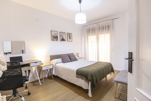 A hotel room with a bed, desk, chair, and a large window with curtains.