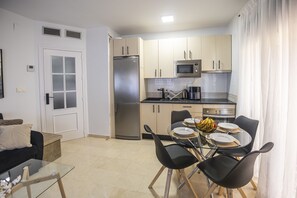 A compact kitchen with a refrigerator, microwave, and dining area with chairs and a table.