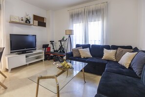 Ein Wohnzimmer mit Fernseher, Sofa, Couchtisch und Heimtrainer.