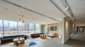 Un vestíbulo amplio con diseño moderno, que incluye una zona de estar con sofás y mesas, grandes ventanales con vista a la ciudad y una estética limpia y minimalista.
