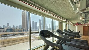 Un gimnasio con cintas de correr, amplias ventanas y vistas a un paisaje urbano.