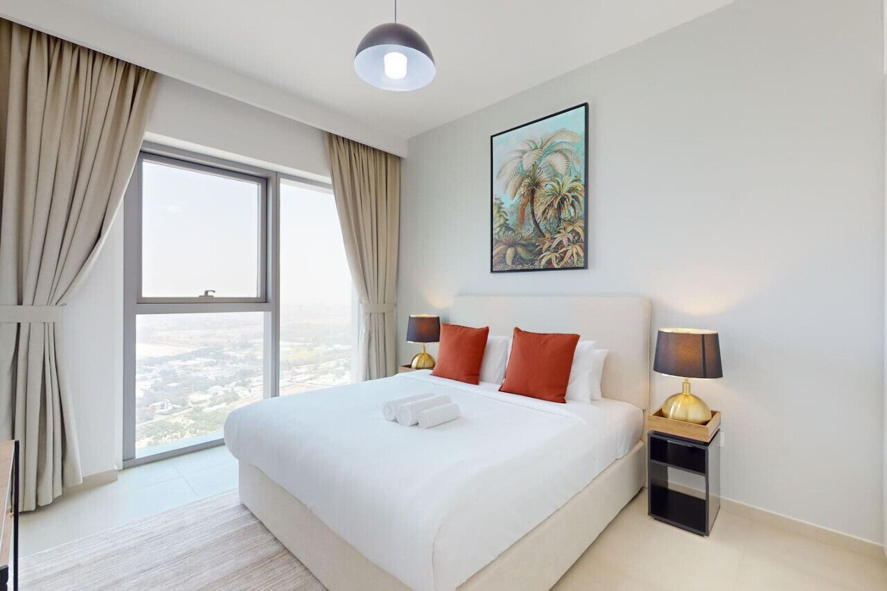 A hotel room with a large bed, two bedside lamps, a nightstand, a painting on the wall, and a view through the window.