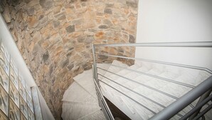A stone-walled stairwell with a metal handrail and a tiled floor.