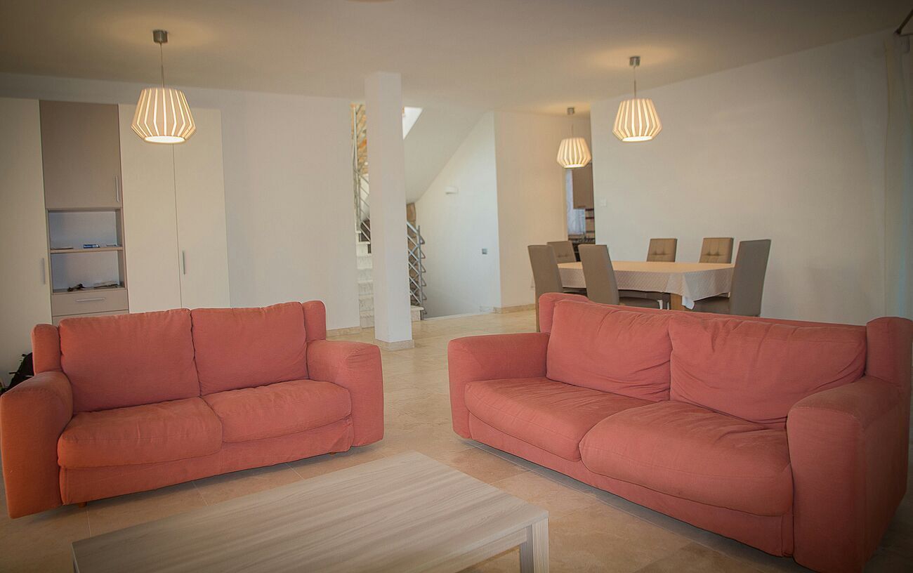 A modern living room with two orange sofas, a wooden coffee table, and a dining area with a table and chairs.