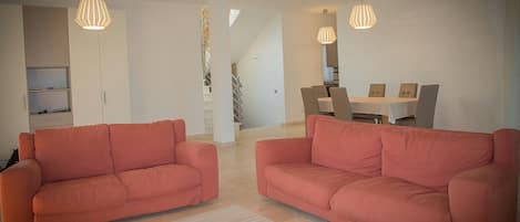 A modern living room with two orange sofas, a wooden coffee table, and a dining area with a table and chairs.