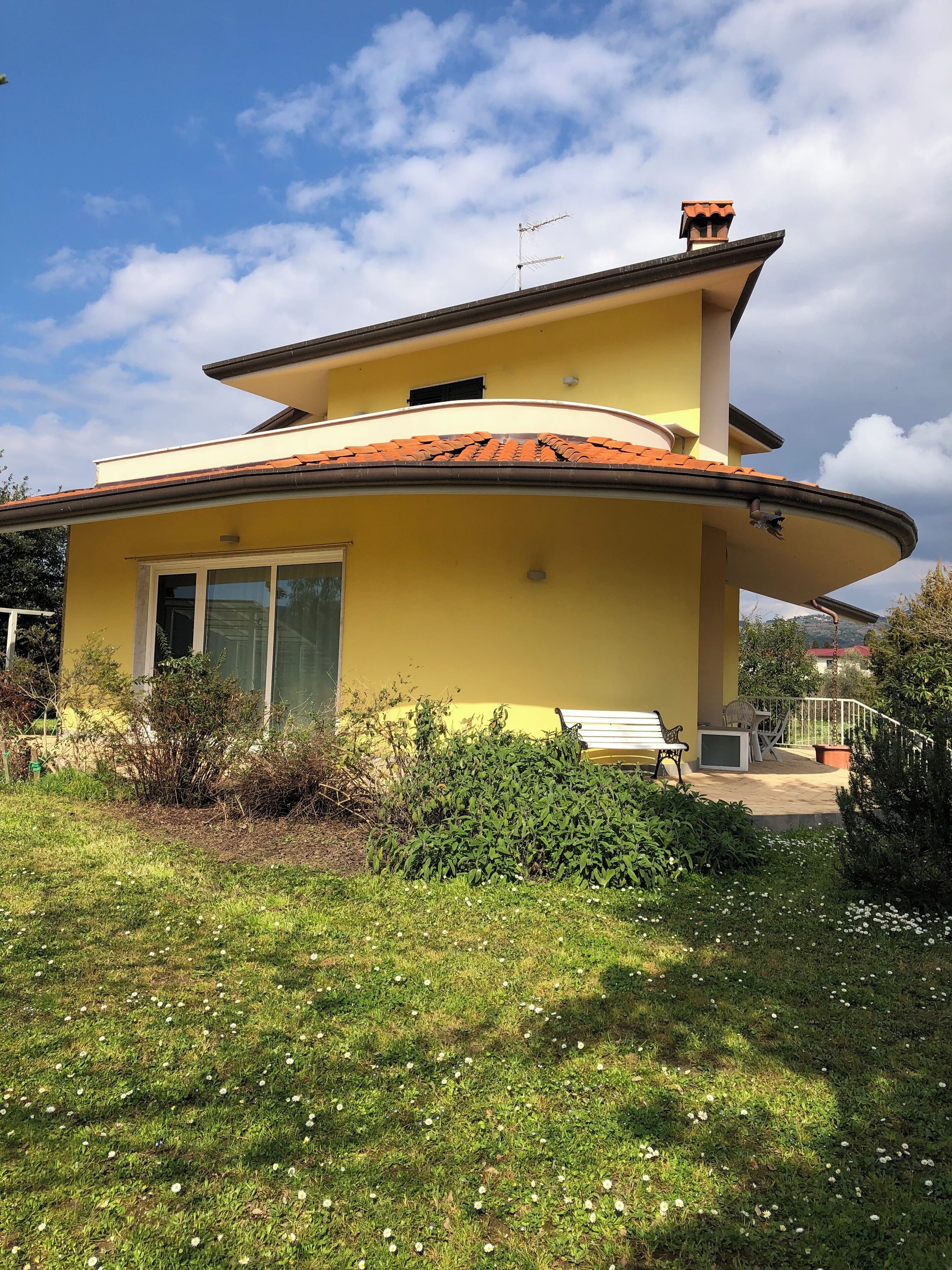 Una casa de dos pisos con techo curvo, una chimenea y un balcón con mobiliario exterior.