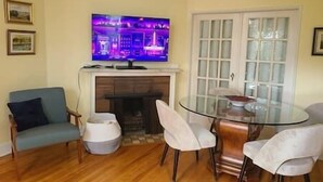 Un salon doté d’une cheminée, d’un téléviseur fixé au-dessus, d’une table en verre avec des chaises, et d’une porte dont les panneaux sont en verre dépoli.