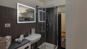 A modern bathroom with a glass-enclosed shower, a white sink, and a mirror above it. - Superba Studio by Wonderful Italy (Genoa)