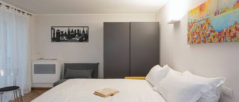 A hotel room with a bed, a chair, a wardrobe, and a painting on the wall.