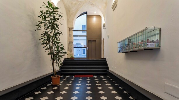 A hallway with a checkered floor, a potted plant, and a glass display case on the wall. - Superba Studio by Wonderful Italy (Genoa)