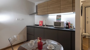 A compact kitchen with wooden cabinets, a microwave, a kettle, and a small dining table with a chair. - Superba Studio by Wonderful Italy (Genoa)