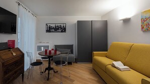 A modern living room with a yellow sofa, a dining table with chairs, a grey couch, a wooden cabinet, and a black and white cityscape artwork on the wall. - Superba Studio by Wonderful Italy (Genoa)
