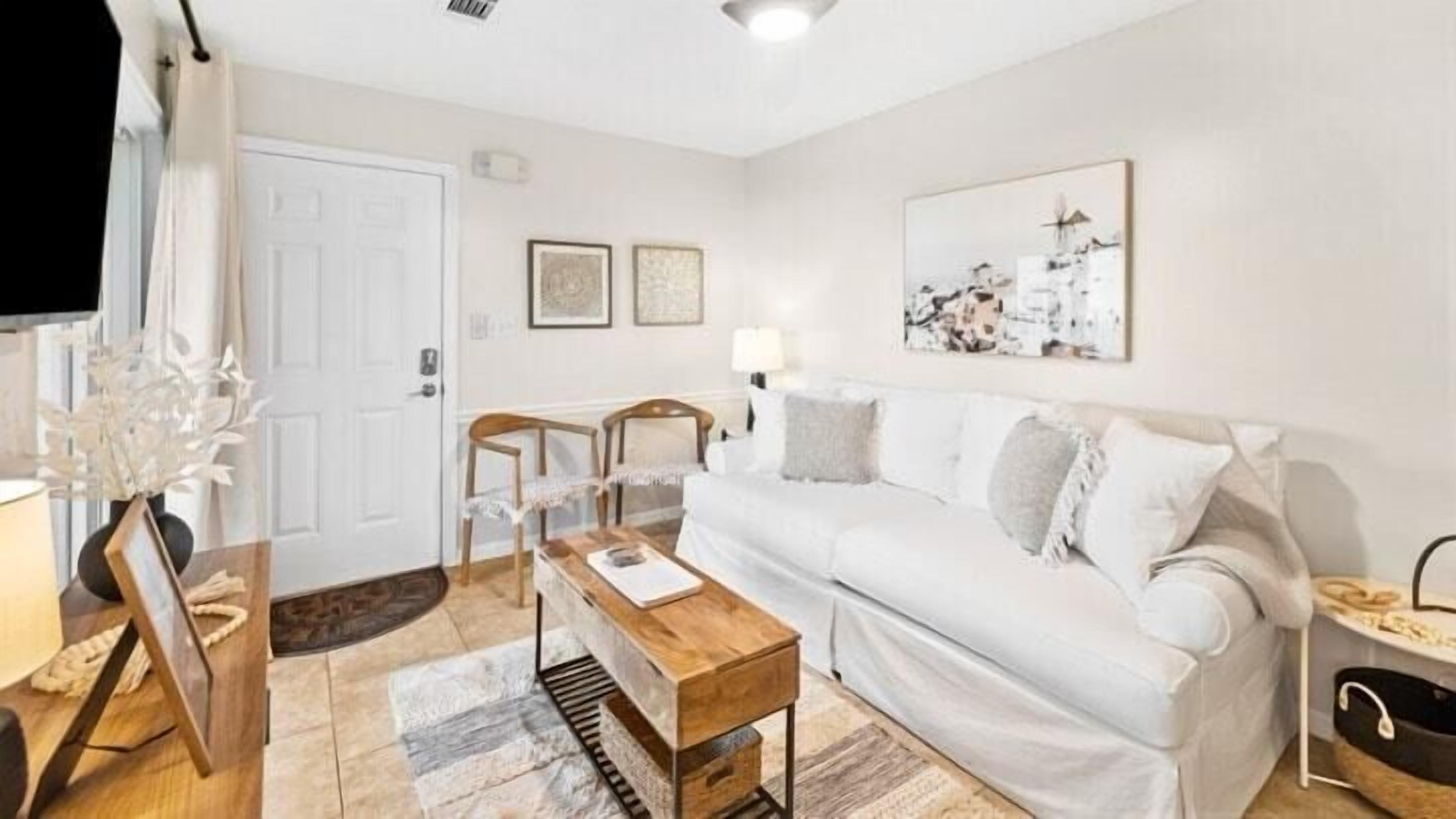 A white living room with a wooden coffee table, a white sofa, and a framed picture on the wall.