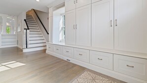 Et rummeligt værelse med en stor, hvid garderobe, en trætrappe og et mønstret tæppe.