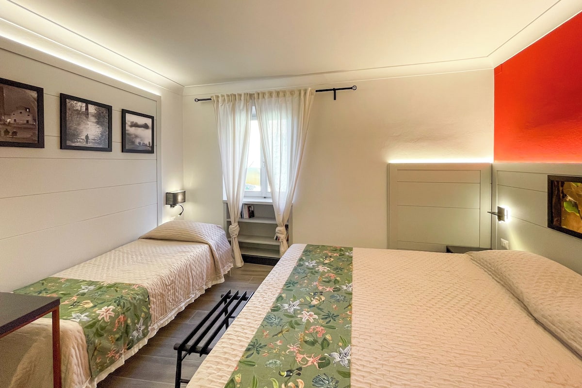 A bedroom with two single beds, a window with curtains, a staircase, and framed pictures on the wall.