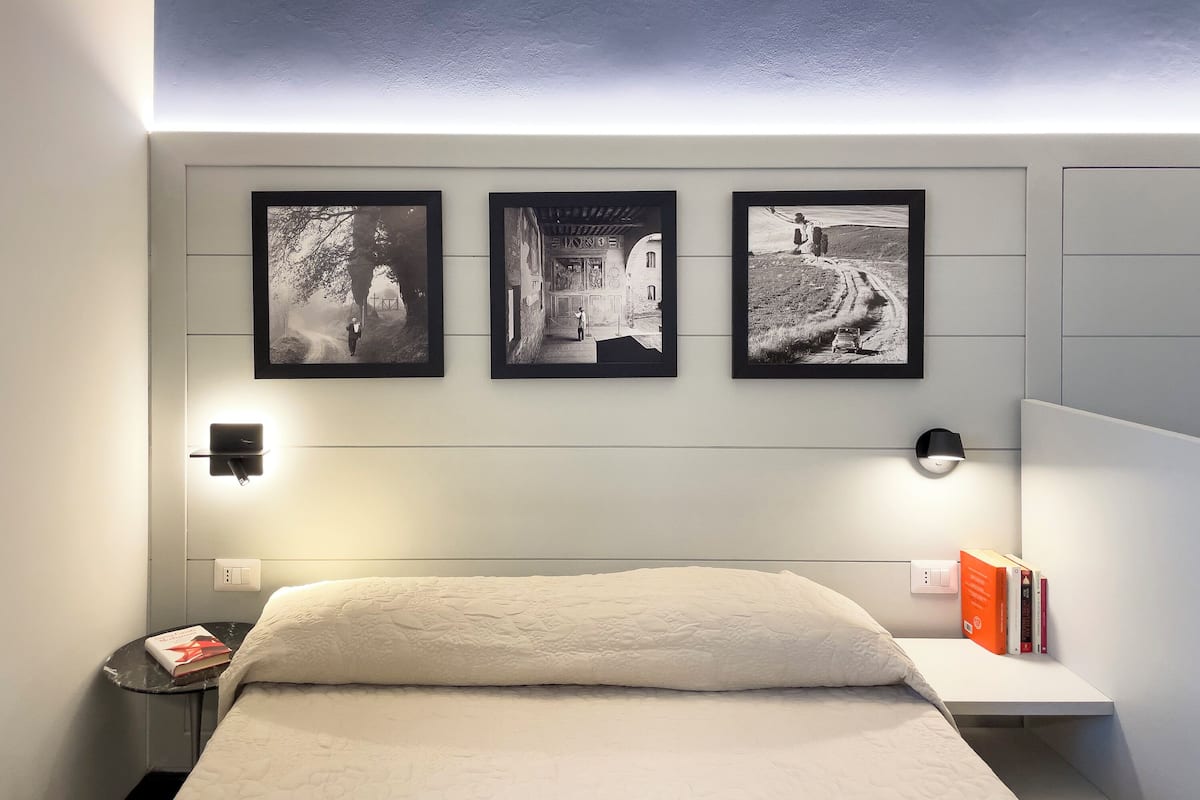 A bedroom with a bed, a bedside table with a book, a nightstand, and three framed pictures on the wall.