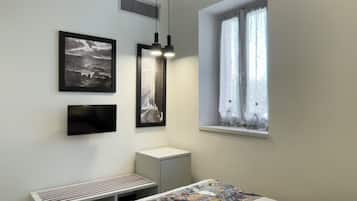 Quarto com cama, um banquinho, janela com cortinas e duas luzes fixadas na parede.